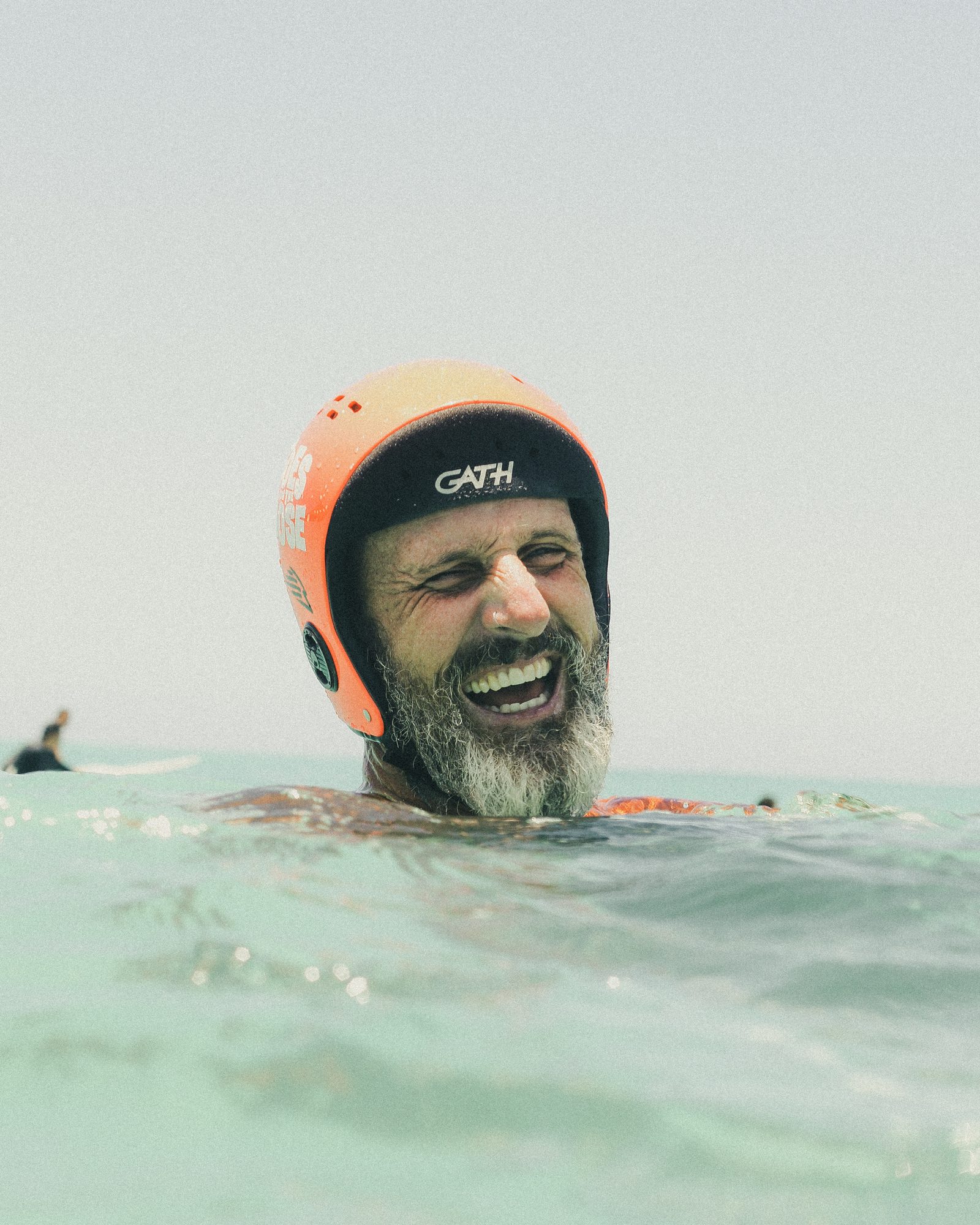 Tommy Pierucki laughing in the water in his orange Gath helmet between waves.